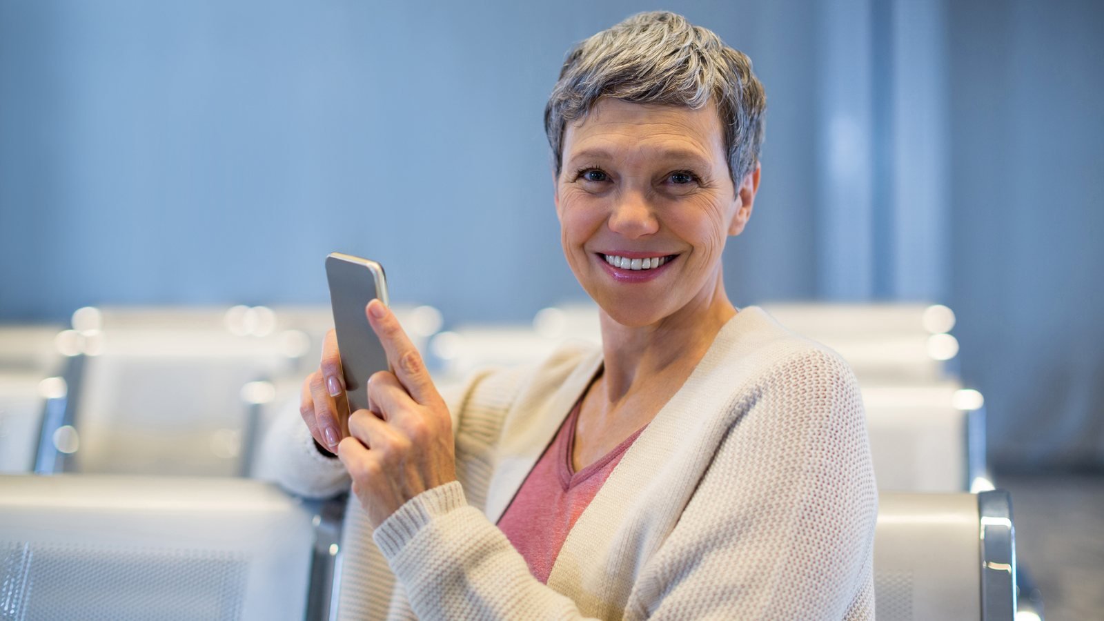 Smiling woman holding a smartphone while sitting in a waiting area